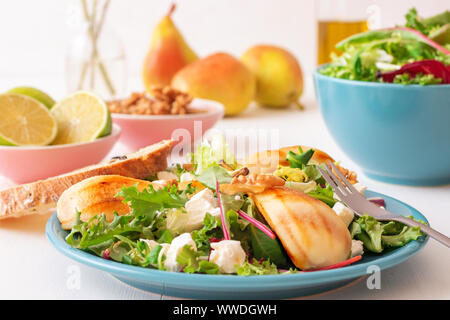 Bianco tavolo in legno di noce con insalata di pere caramellate e formaggio feta. Turquise piatti con insalata, fette di twisted Il pane svizzero con olive, limets Foto Stock