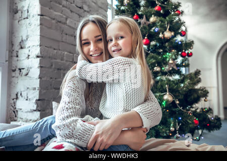 Felice Giovane Donna con bambina carina seduta sul letto di casa, godendo di famiglia, tradizionali decorazioni di Natale e Anno Nuovo concetto di vacanze Foto Stock