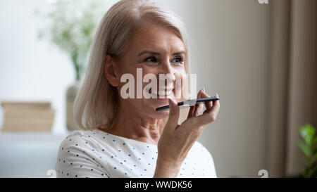 Sorridente donna matura la registrazione del messaggio vocale sul telefono vicino fino Foto Stock
