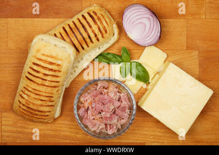 Panini e gli ingredienti, formaggio, prosciutto cotto, cipolla rossa e basilico su un tagliere di legno Foto Stock