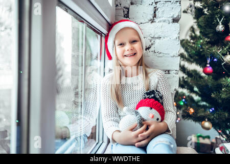 Un bambino piccolo che si siede su un davanzale. Concetto Felice Natale e Anno Nuovo, vacanza invernale, infanzia. Foto Stock