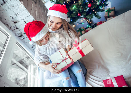 Una bambina con la sua mamma si apre un nuovo anno di dono vicino a una festa di Natale albero. vista superiore Foto Stock