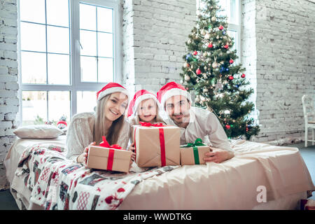 Famiglia nel Natale cappelli di Babbo Natale giacente sul letto. Padre madre e bambino divertirsi in camera da letto. Le persone in un momento di relax a casa. Vacanza invernale Natale e Anno Nuovo c Foto Stock