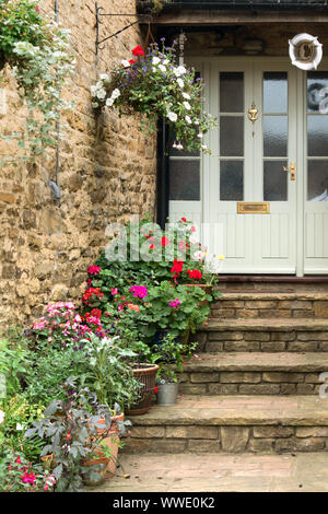 Piuttosto di gradini di pietra che conduce fino a casa lo sportello anteriore con piantatrici, nei cestini appesi e piante fiorite, Easton sulla collina,Northamptonshire, England, Regno Unito Foto Stock