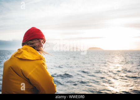 Anone uomo traveler galleggiante sulla nave guardando il tramonto mare dopo la tempesta e le montagne di nebbia sulla skyline. Lo stile di vita all'aperto di viaggio scandinavian autentica Foto Stock