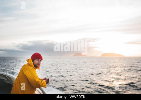 Anone uomo traveler galleggiante sulla nave guardando il tramonto mare dopo la tempesta e le montagne di nebbia sulla skyline. Lo stile di vita all'aperto di viaggio scandinavian autentica Foto Stock