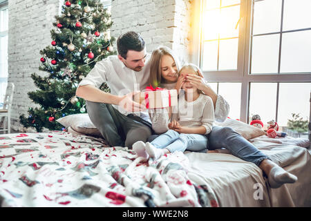 Buon Natale e Buone Feste!!! Allegro padre, madre e la sua figlia carina ragazza lo scambio di doni. Genitore e bambino divertirsi vicino a Chris Foto Stock