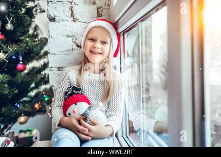 Un bambino piccolo che si siede su un davanzale. Concetto Felice Natale e Anno Nuovo, vacanza invernale, infanzia. Foto Stock