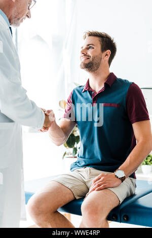 Felice paziente stringono le mani con barbuto medico in camice bianco Foto Stock