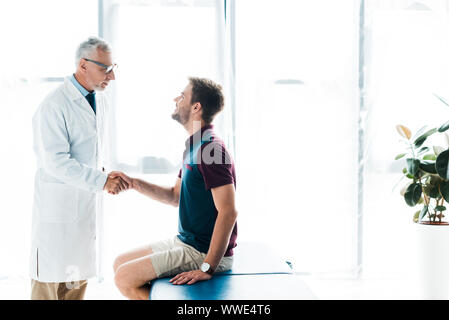 Dottore in bicchieri stringono le mani con uomo felice in clinica Foto Stock