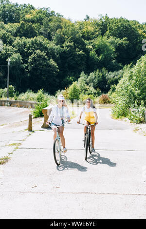 Felice bionda e bruna girls riding bike in estate Foto Stock