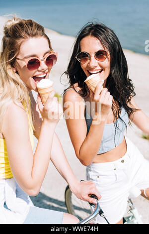 Felice bionda e bruna ragazze equitazione biciclette e mangiare il gelato Foto Stock