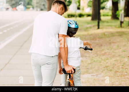 Vista posteriore del padre aiutando figlio di correre in bicicletta mentre il bambino seduto sulla bici Foto Stock