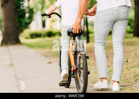 Vista ritagliata del padre aiutando figlio di correre in bicicletta mantenendo sit di bike Foto Stock