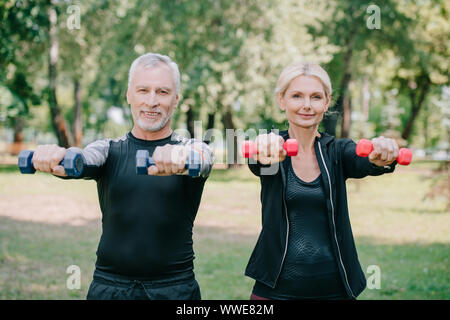 Sorridente sportivo maturo e sportive a fare gli esercizi con barbells e sorridente in telecamera Foto Stock