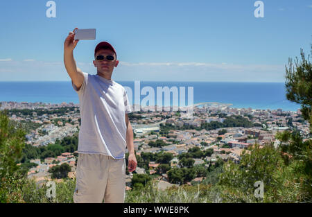 Un uomo parla su un telefono cellulare, rende le videochiamate mentre su una montagna in riva al mare Foto Stock