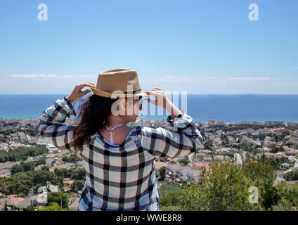 Una giovane bella bruna ragazza in un cappello sorge su una montagna ai piedi di una montagna Foto Stock