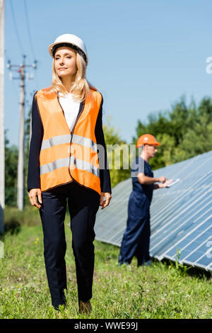 Attraente imprenditrice nel hardhat camminando e guardando lontano Foto Stock