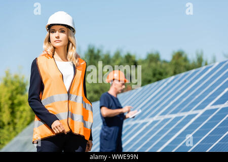 Attraente imprenditrice nel casco e giubbotto di sicurezza che guarda lontano Foto Stock