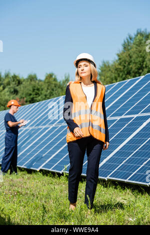 Attraente imprenditrice nel hardhat camminando e guardando lontano Foto Stock