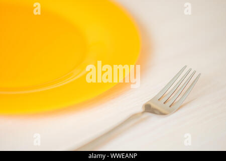 Piastra di colore arancione e la forcella closeup sulla luce tavolo in legno. Foto Stock