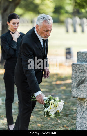 Messa a fuoco selettiva di senior uomo mettere fiori vicino alla tomba e donna Foto Stock