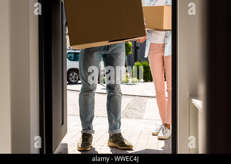 Vista ritagliata di un uomo e di una donna di scatole di contenimento mentre si cammina in casa Foto Stock