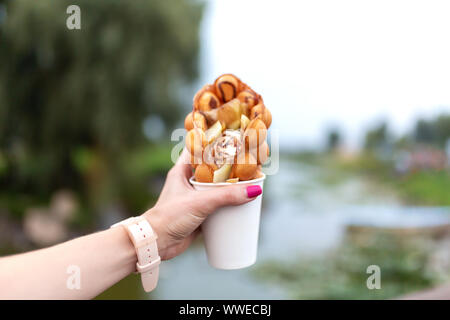 La ragazza durante la passeggiata che tiene in mano un bicchiere di carta con una cialda belga su uno sfondo di green park. Foto Stock