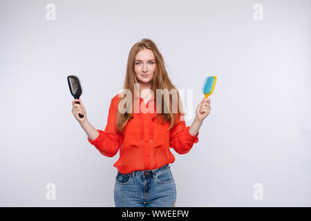 Donna che mantiene due spazzola per capelli in posa con una metà shaggy e capelli pettinati medium shot Foto Stock