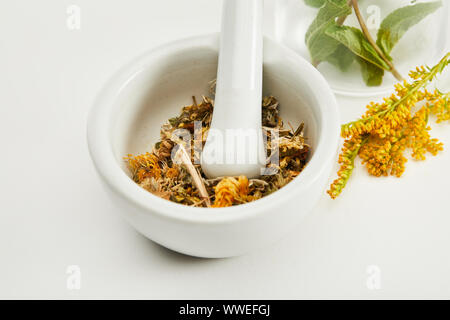 Mortaio e pestello con mix di erbe vicino ramoscello oro su sfondo bianco Foto Stock