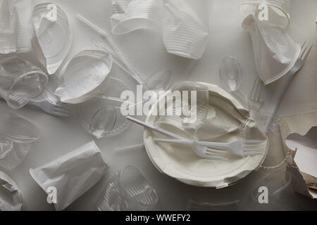 Vista dall'alto di accartocciata piastre monouso, i bicchieri di plastica, forchette e cucchiai su sfondo bianco Foto Stock