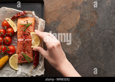 Vista ritagliata della donna spremendo il succo di limone su crudo bistecca di salmone con verdure sul vassoio del forno Foto Stock