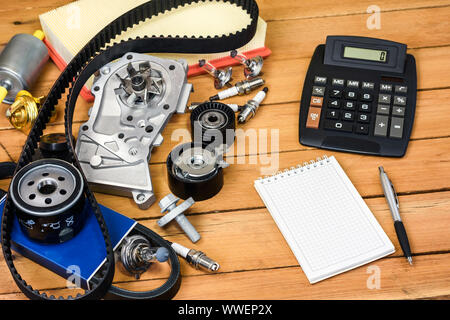 Varie parti di automobili con la calcolatrice, un blocco e una punta a sfera matita sul tavolo di legno. Foto Stock