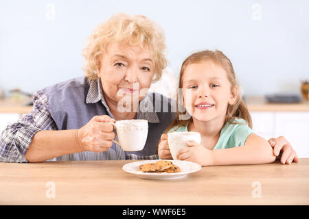 Carino bambina e la nonna bere il tè con biscotti in cucina Foto Stock