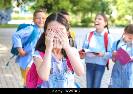 Little Schoolgirl che copre gli occhi con le mani all'aperto Foto Stock