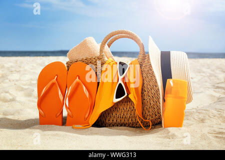 Borsa con flip-flop, costume da bagno, cappello, occhiali da sole e cosmetici e sulla spiaggia di sabbia Foto Stock