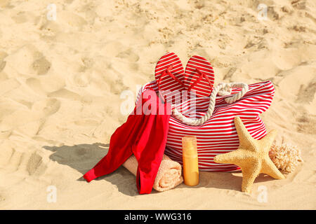 Borsa con flip-flop, costume da bagno e asciugamano e cosmetici e sulla spiaggia di sabbia Foto Stock