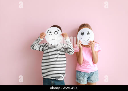 Figlioli volti nascosti dietro le emoticon disegnata sul colore di sfondo Foto Stock