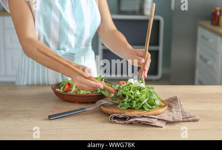 Donna mettendo una gustosa insalata di rucola sulla piastra sulla tavola in cucina Foto Stock