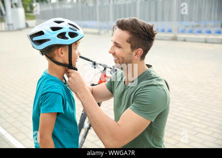 Padre aiutando il suo figlio a mettere il casco prima bicicletta equitazione all'aperto Foto Stock