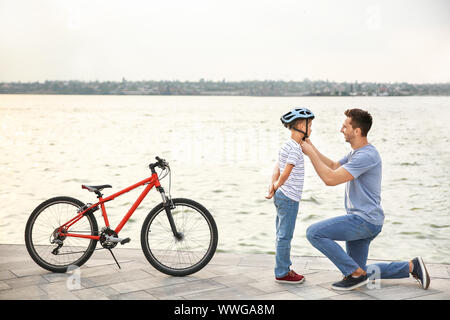 Padre aiutando il suo figlio a mettere il casco prima bicicletta equitazione all'aperto Foto Stock