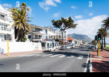 Camps Bay, elegante sobborgo di Cape Town, Sud Africa, guardando in giù la strada principale a negozi, ristoranti ed edifici di appartamenti in un giorno di primavera Foto Stock