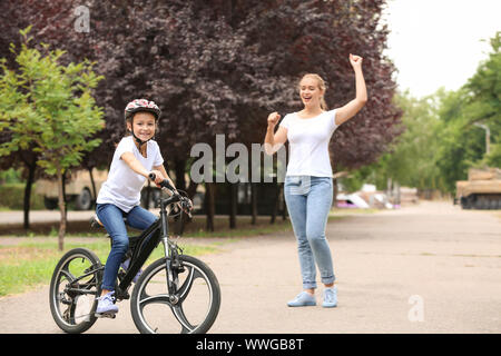 Madre orgogliosa di sua figlia che ha imparato a guidare la bicicletta all'aperto Foto Stock