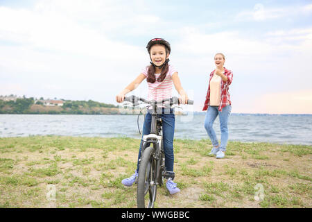 Madre orgogliosa di sua figlia che ha imparato a guidare la bicicletta all'aperto Foto Stock