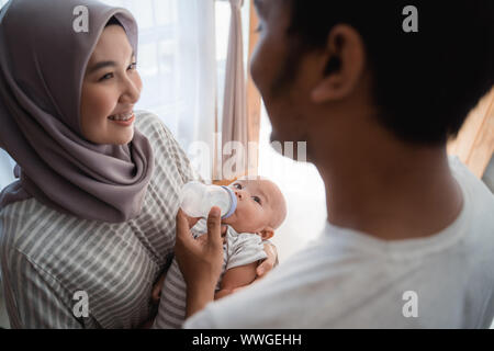 Asian genitore bambino alimentazione con bottiglia di latte insieme a casa Foto Stock