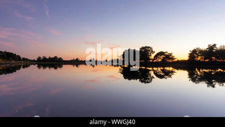 Sunset over Hatchet stagno, New Forest, Hampshire REGNO UNITO mostra sagome di alberi in acqua ancora Foto Stock