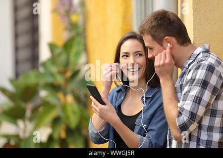 Coppia felice condivisione di auricolari per ascoltare la musica online da smart phone in un colorato street Foto Stock