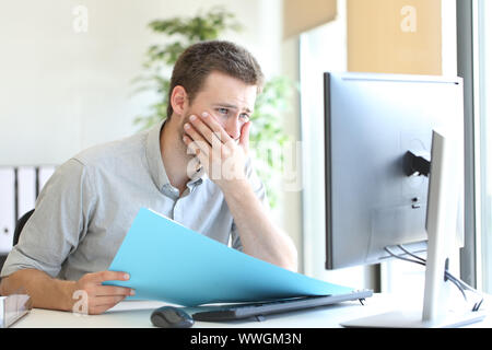 Imprenditore preoccupati alla scoperta di errore confrontando le informazioni sul documento e contenuto del computer in ufficio Foto Stock