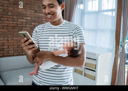 Padre che porta la figlia quando si utilizza lo smartphone in casa Foto Stock