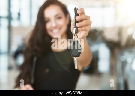 Bella donna manager sorridente azienda brochure in una mano e le chiavi dell'auto in un altro in piedi nel centro della concessionaria Foto Stock